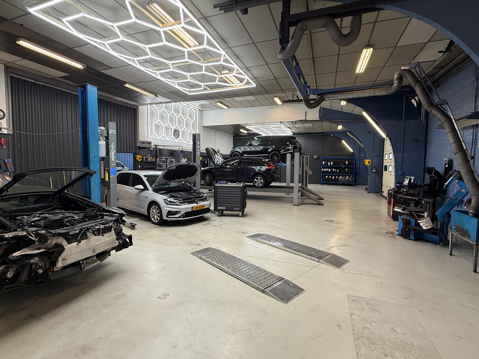 Het ruime, moderne werkplaatsinterieur van Comfort Fit Zevenaar met auto's op de hefbrug